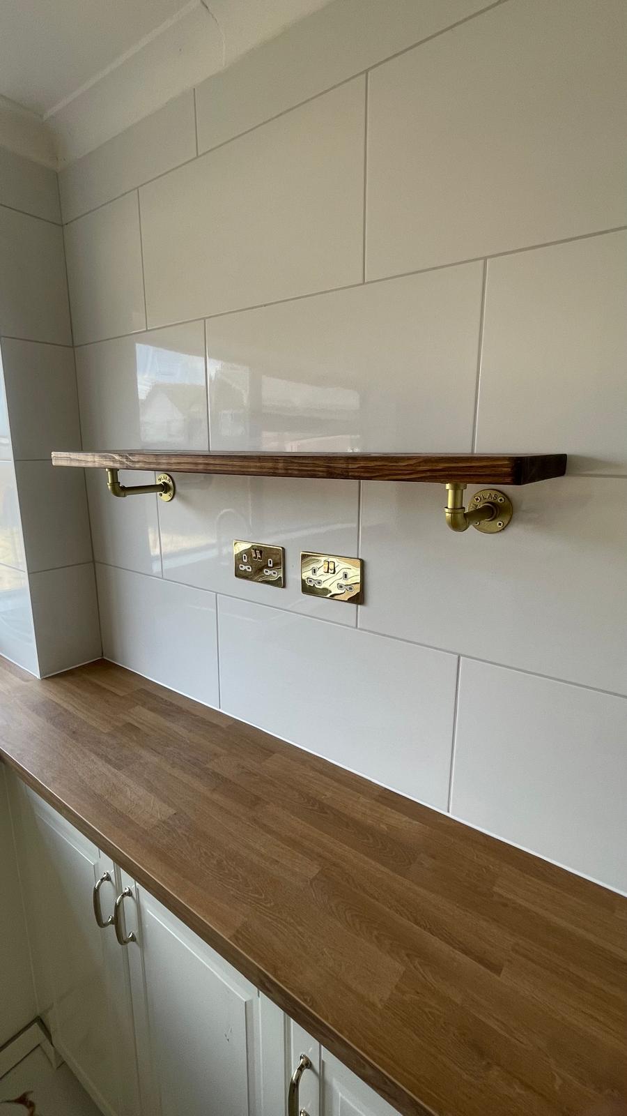Oak worktop with brass pipe bracket shelf and brass sockets on white tiled wall in Park Hall kitchen