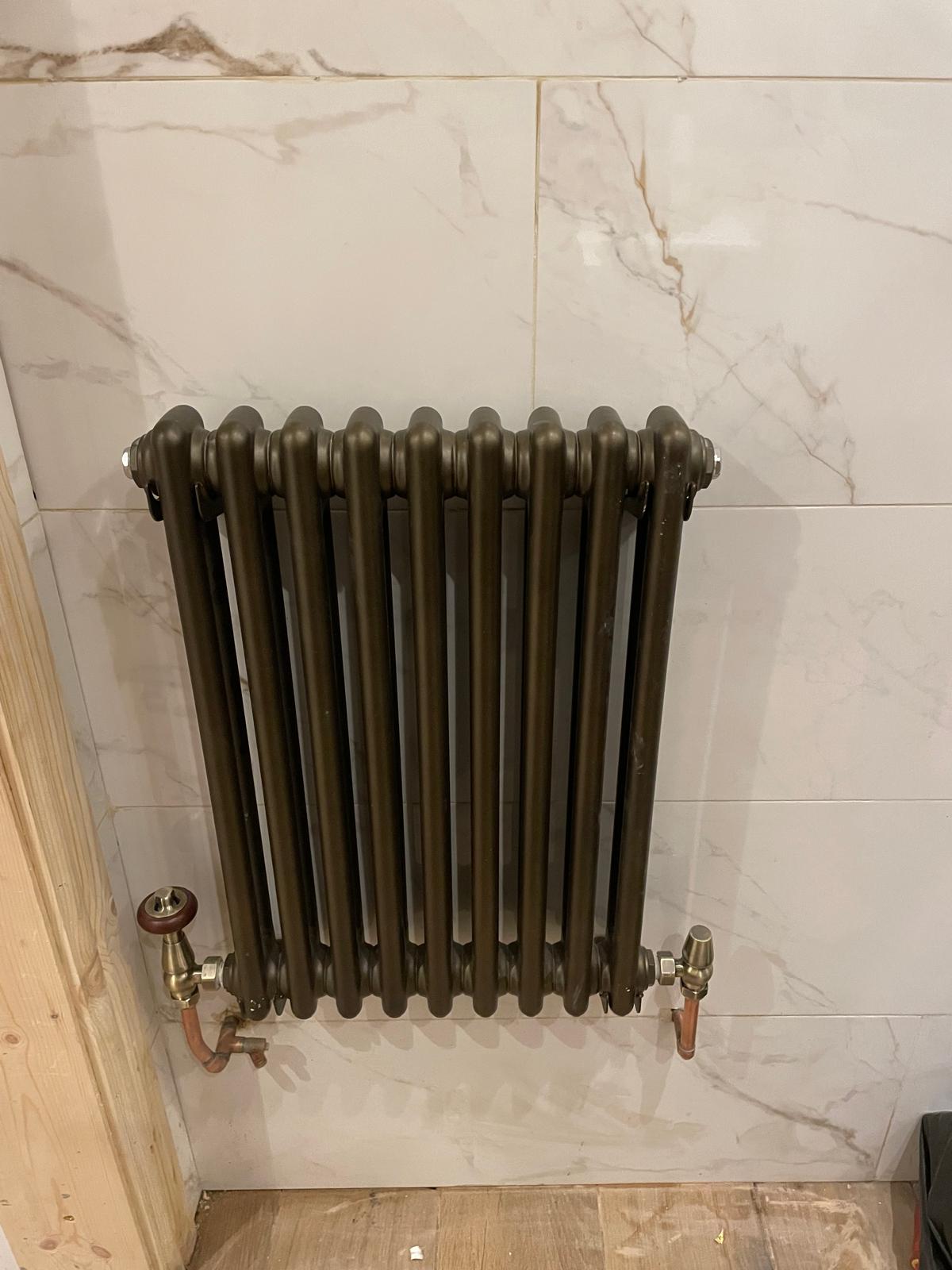 Bronze column designer radiator with brass valves installed on marble-effect tiles in a Wednesbury kitchen